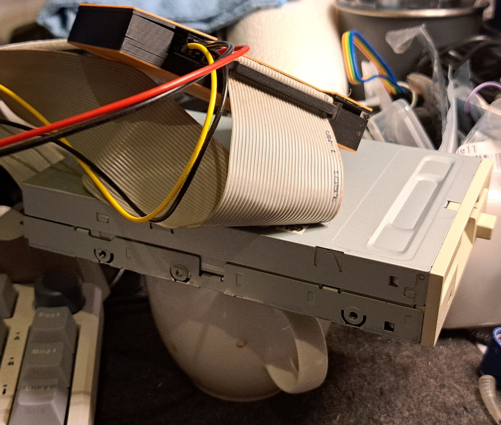 Greaseweazle V4.1 im orange-schwarzen 3D-Druck-Gehäuse, per Flachbandkabel und 4-Pin-Stromkabel an einem beigen 3,5-Zoll-Diskettenlaufwerk